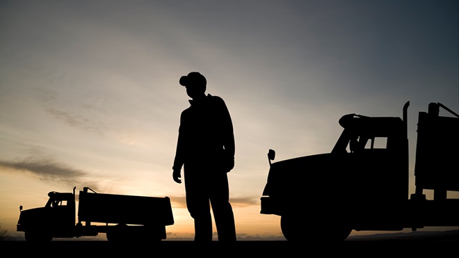 truck driver standing beside his truck in shadow